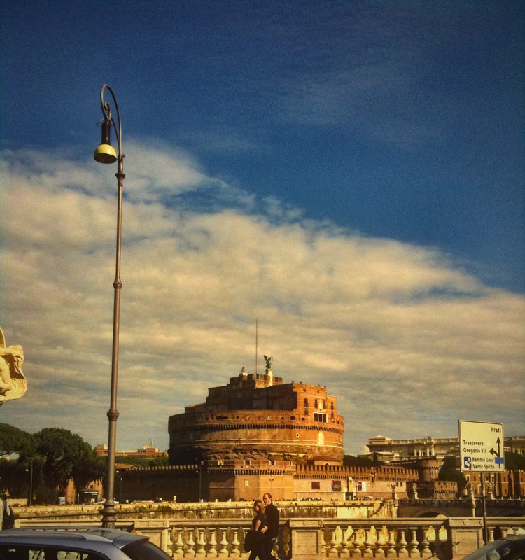 A tall lamp post with Castel Sant'Angelo behind under streaked clouds.