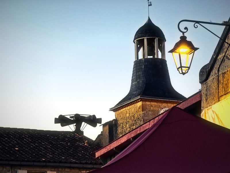 A slate bell cupola beside a glowing street lantern under a pale evening sky.