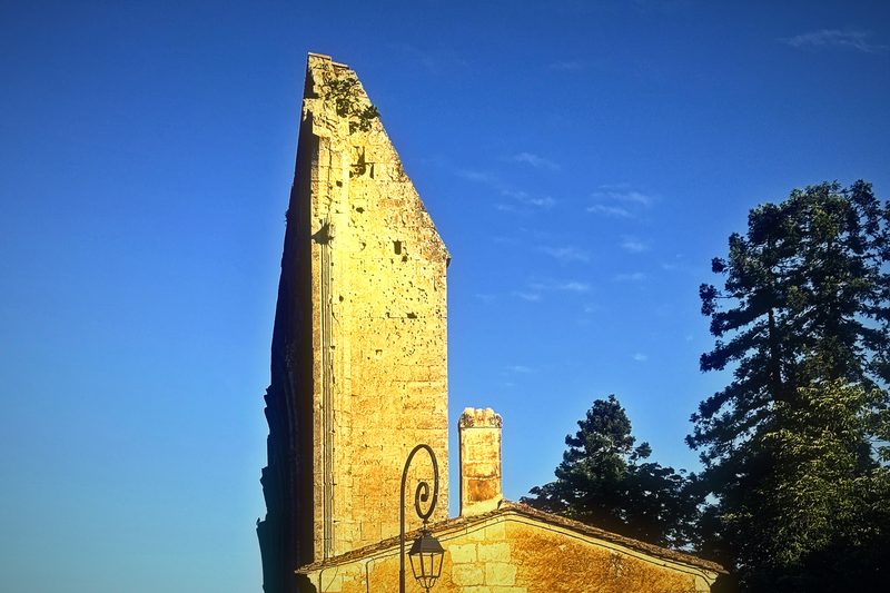 A tall ruined stone tower lit gold by low morning sun against a clear sky.