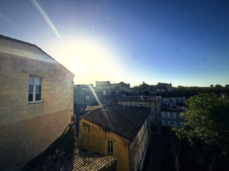 The morning sun flaring over tiled roofs and stone walls in a hilltop town.