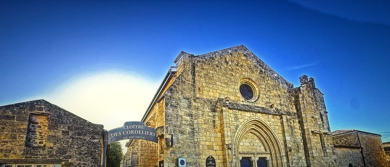Low morning sun flaring beside the weathered façade of an old stone church on a quiet square.