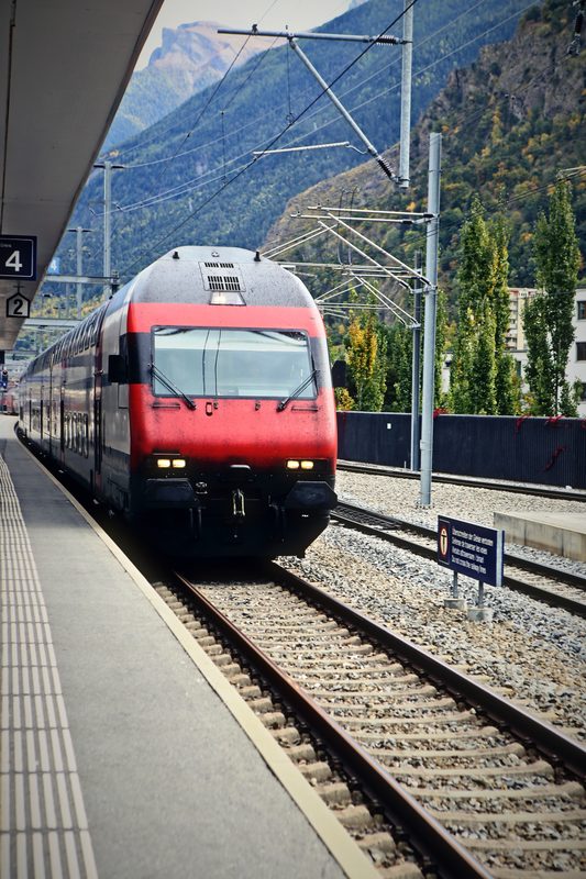 Red Swiss locomotive approaching a platform with steep mountains behind.