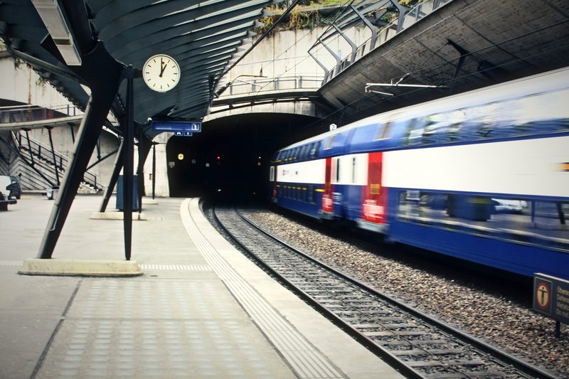 Station platform under curving steel ribs, a clock overhead and a blue double-deck train in a tunnel mouth.