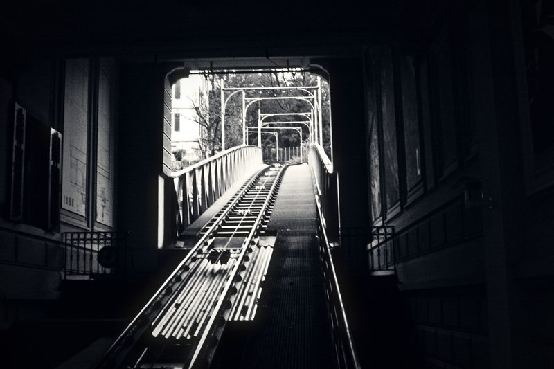 Funicular track rising through a dark tunnel toward a bright opening.