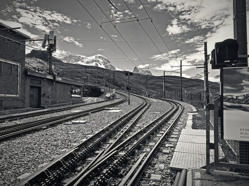 Black and white rack railway tracks curving uphill beside a small station.