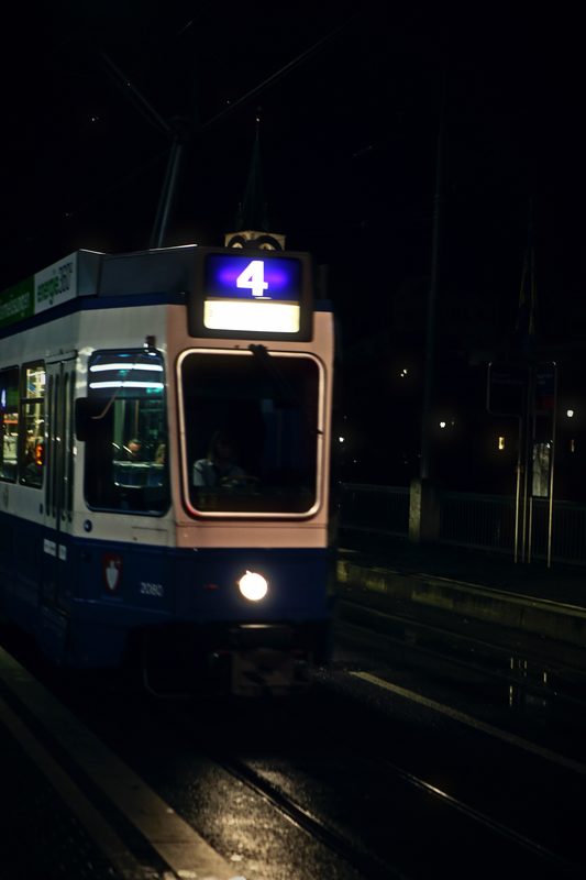 Zürich tram with a glowing number 4 sign arriving at night.