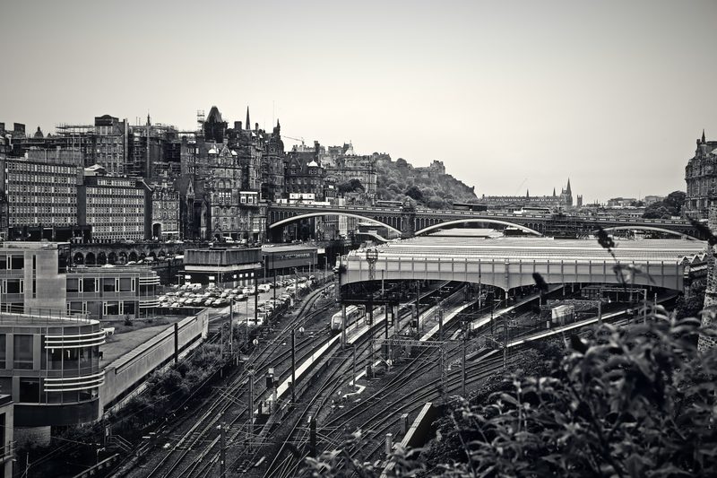 Black and white view down onto station roofs and tracks with the city skyline behind.