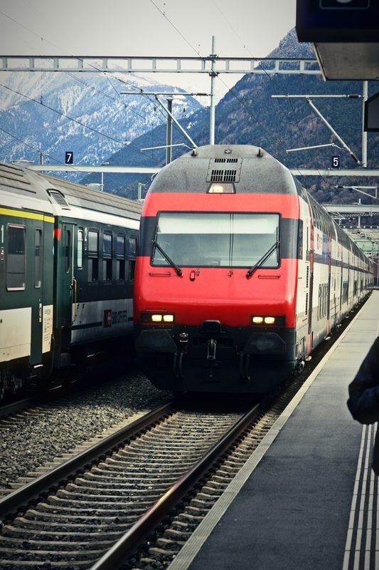 Red Swiss locomotive arriving beside another train with mountains behind.