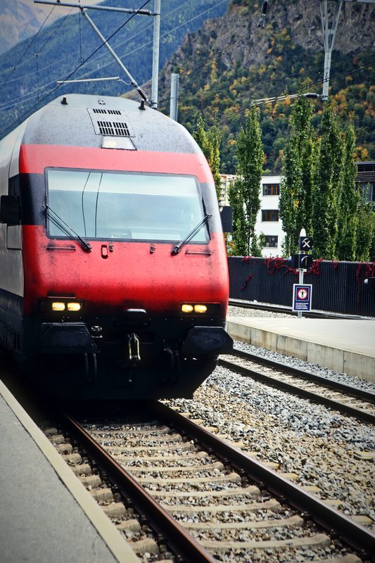 Red locomotive close up at a platform edge with steep green slopes behind.