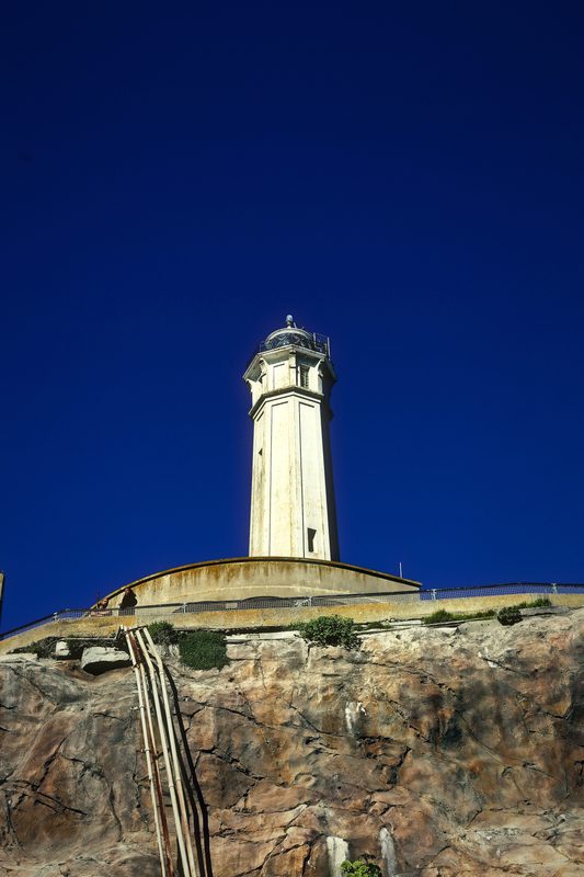 Lighthouse over old concrete walls and rock under a deep blue winter sky.