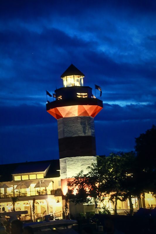 Lit red and white lighthouse against a deep blue evening sky.