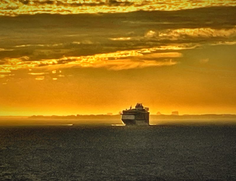 A distant cruise ship on a dark sea beneath a ceiling of glowing gold clouds.