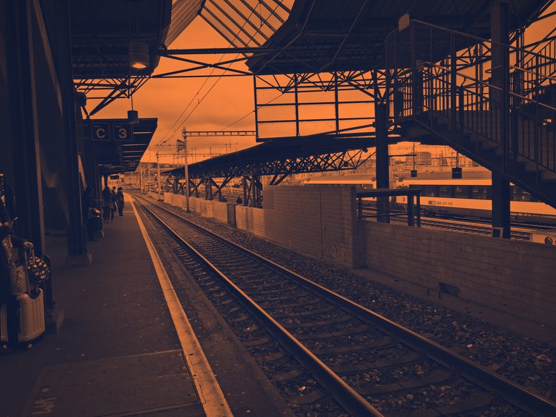 Orange and navy duotone of a station platform with tracks and a canopy.