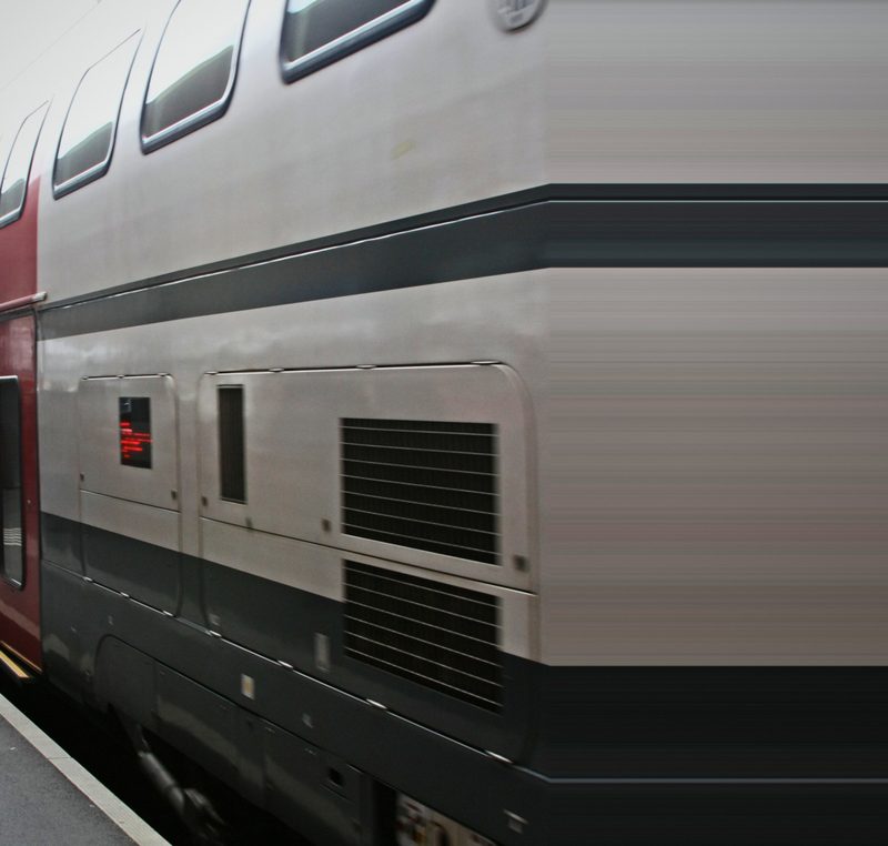 Close abstract of a silver double-deck carriage side with dark bands and vents.