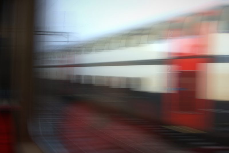 Radial blur of a red and white train leaving a platform.