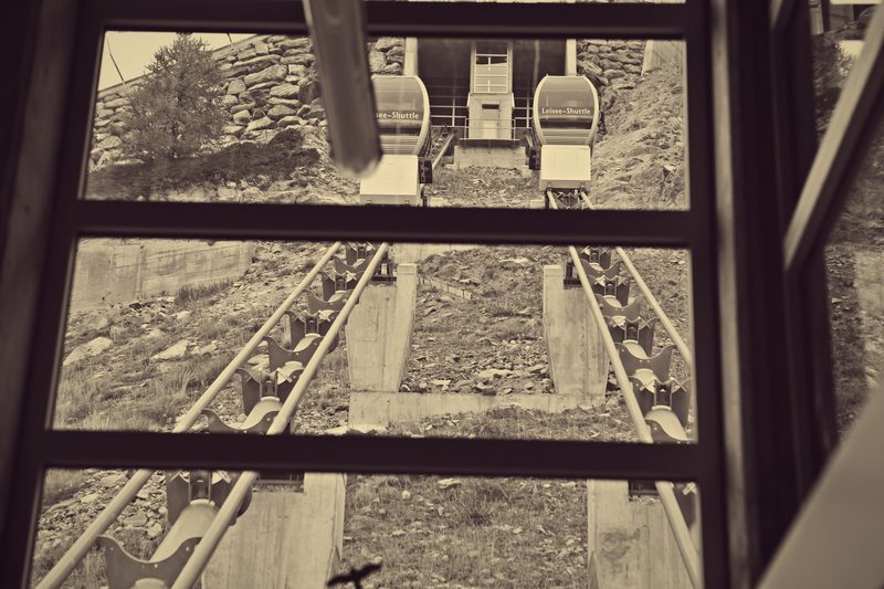 Sepia view through a funicular window down onto parallel tracks and passing cars.
