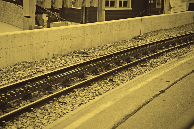 Golden duotone of rails and ballast running beside a concrete wall.