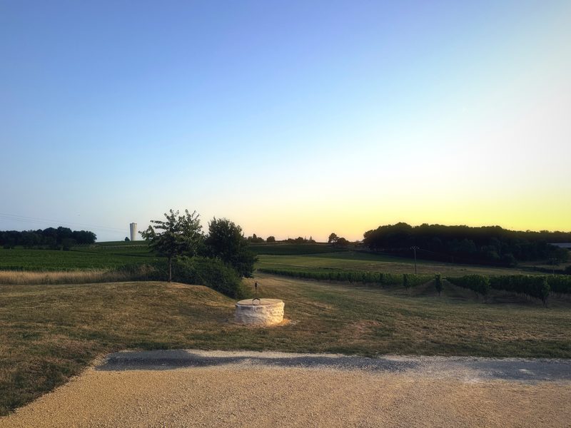 A pale band of afterglow over a dry field, a low wall and a distant tree line.