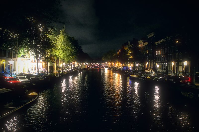 An Amsterdam canal at night with lights reflected in long streaks.