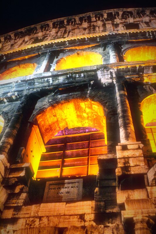 A close view of the Colosseum's arches glowing orange at night.