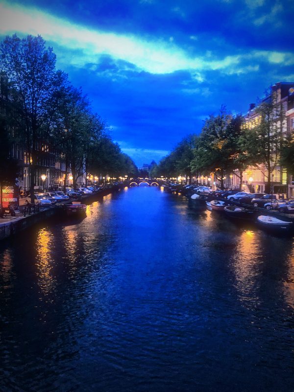 A canal at blue hour, boats moored under a deep blue sky with gold windows.