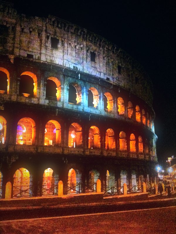 The Colosseum at night from a low angle, tiers lit warm and cool.