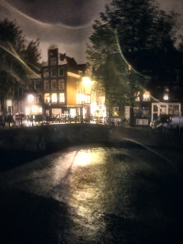 A rainy canal-side lane at night with lights reflecting on wet stone.