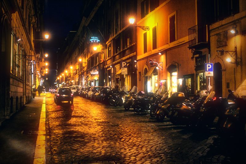 A wet Roman street at night, its cobbles glowing gold.