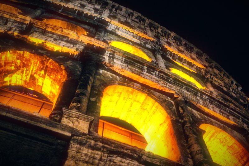 The curved wall of the Colosseum lit orange at night.