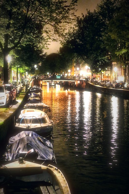 A canal at night with boats and long reflections receding into the dark.