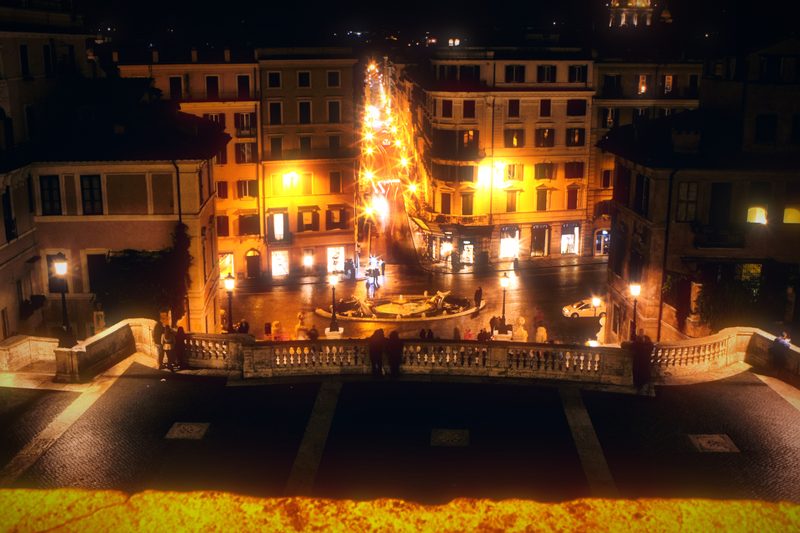 Looking down from a terrace onto a lit street at night.