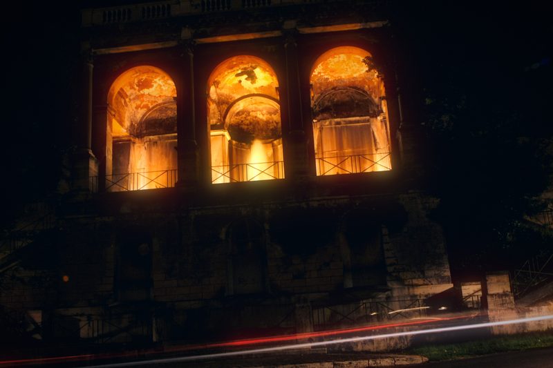 Three arched windows glowing gold in a dark Roman wall, a red streak below.