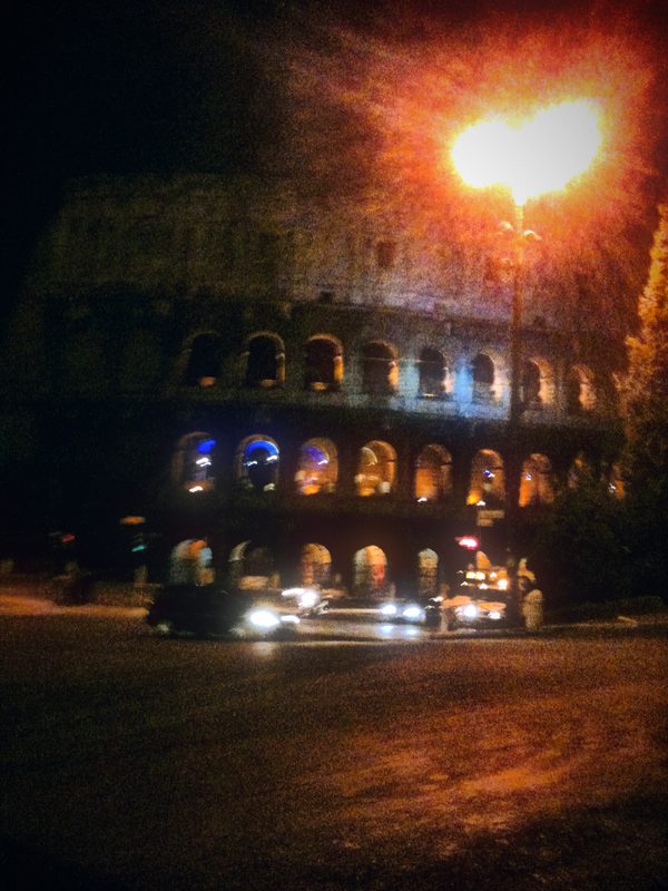 A bright street light and the Colosseum at night above a dark road.