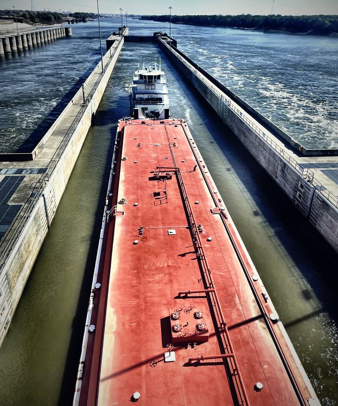 A long red barge squeezed between the concrete walls of a river lock.