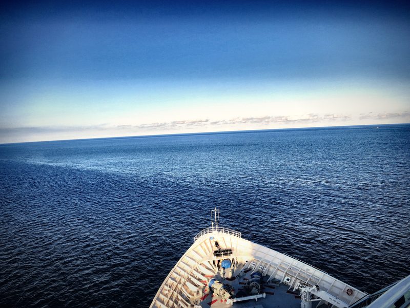 A white ship's bow pointed at a deep blue sea and a hazy horizon.
