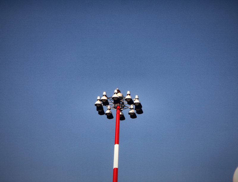 A red-and-white striped floodlight mast against a flat blue sky.