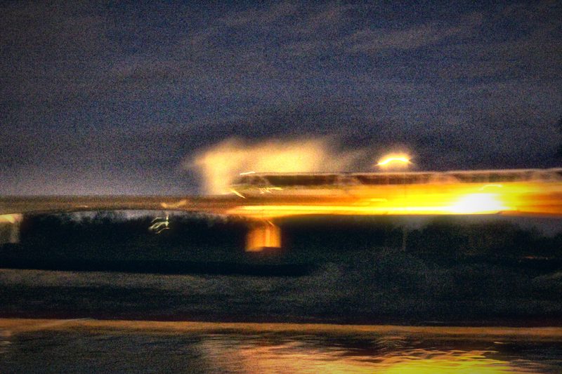 Lights smeared into a fiery horizontal streak over dark water at night.