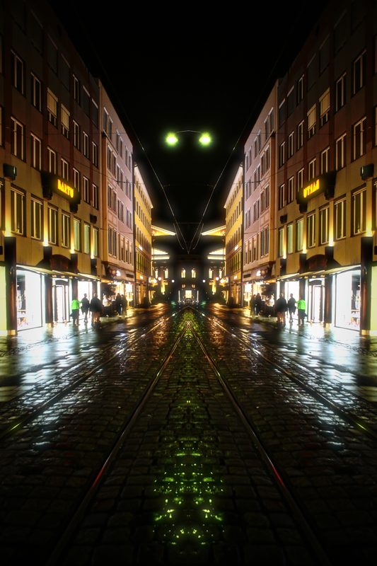 Symmetrical mirrored night street with tram rails meeting in the middle.
