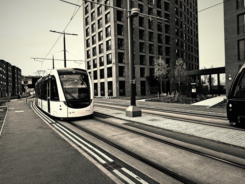 Split-toned image of a tram on a wide street between tall buildings.