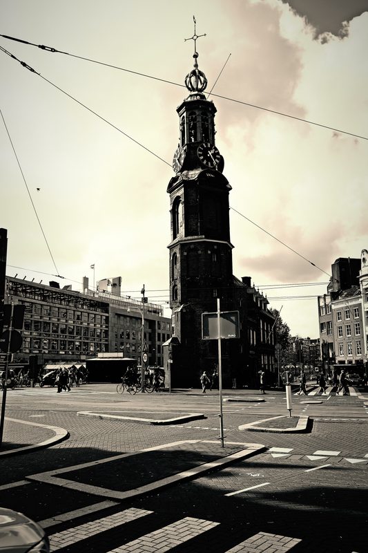 Split-toned clock tower above a tram crossing with wires overhead.