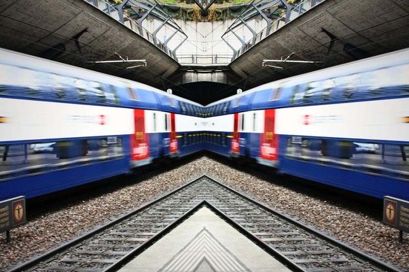Mirrored image of two blue double-deck trains meeting under a canopy.