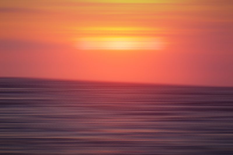 Coral-red sunset band over horizontal streaks of dark sea.