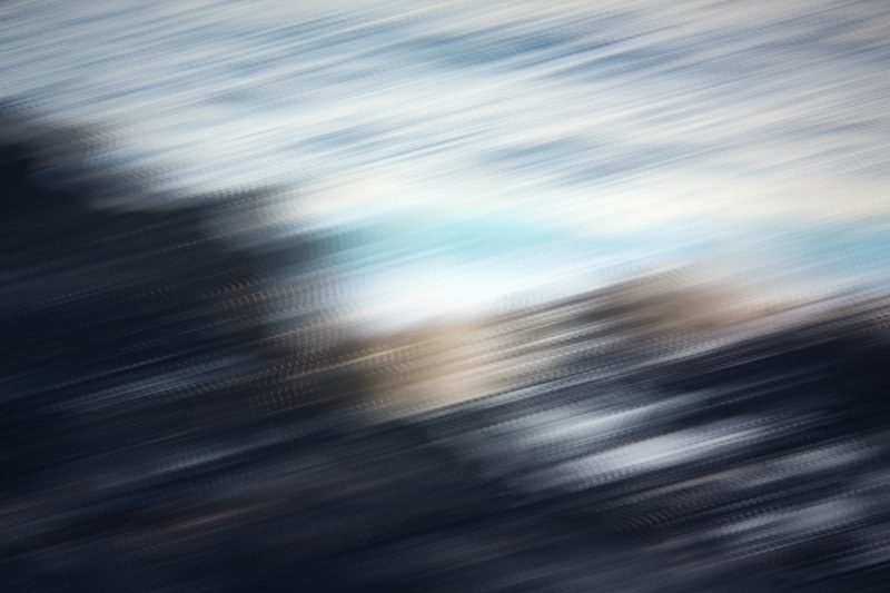 Diagonal streaks of dark rock, white foam and pale sky.