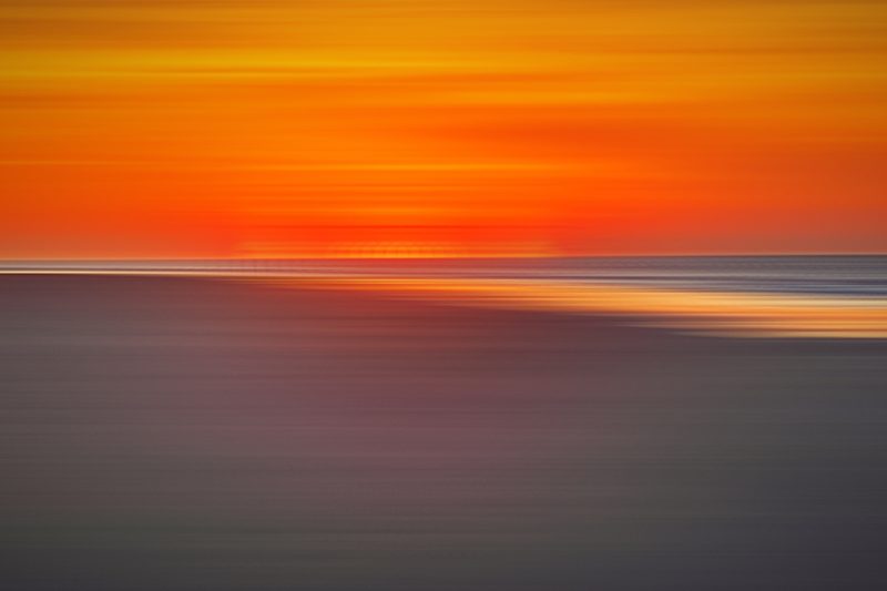 Orange and red sky streaked over dark sand.