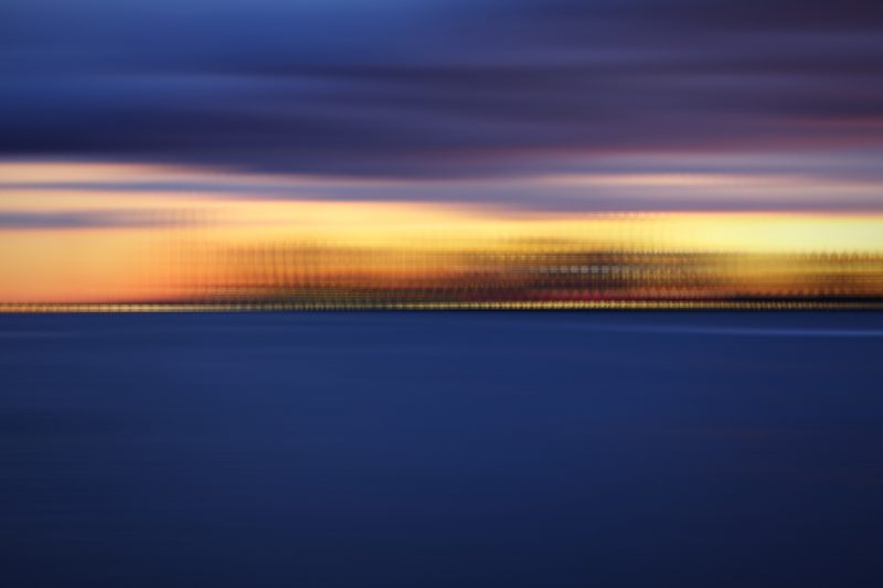 Layered bands of blue, peach and gold sky over dark water.