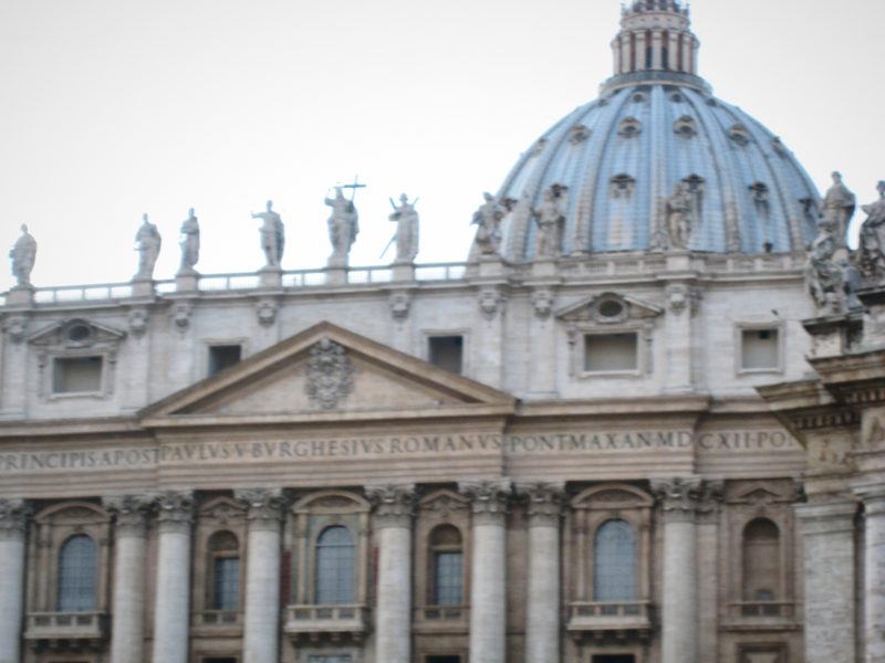 The upper facade of St Peter's with statues and the great dome behind.