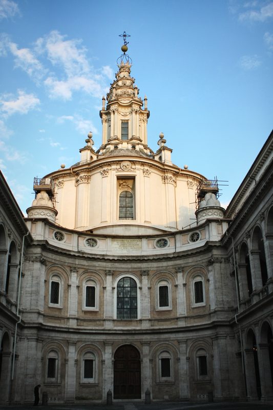 The courtyard and spiral-topped church of Sant'Ivo alla Sapienza under blue sky.