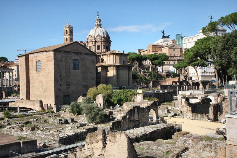 Ruins of the Roman Forum with a church and domes beyond.