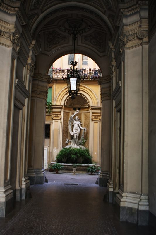 A long arcade leading to a statue in a courtyard niche.