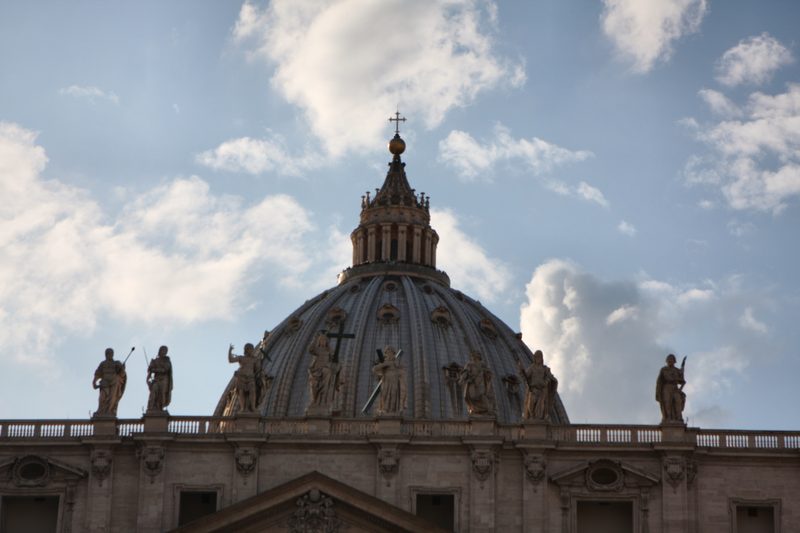 The dome of St Peter's rising above the basilica roofline under cloud.